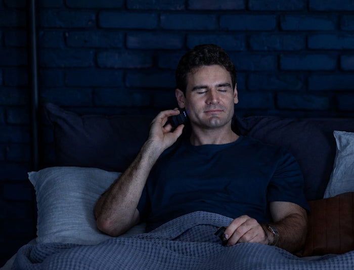 A man lying in bed at night using a Hoolest device and a GABA pouch as part of his wind-down routine.