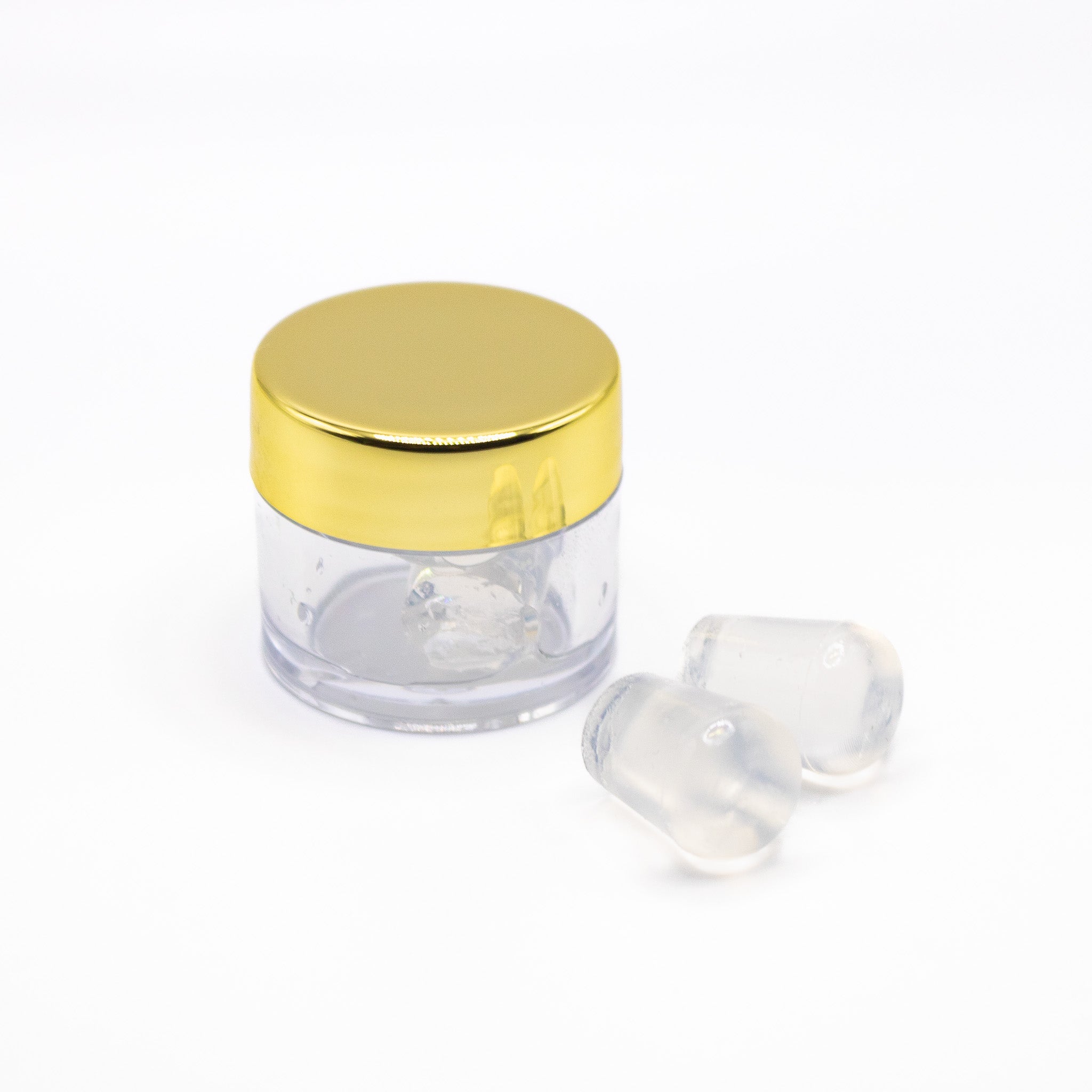 A small jar with a gold lid and two clear capsules on a white background.